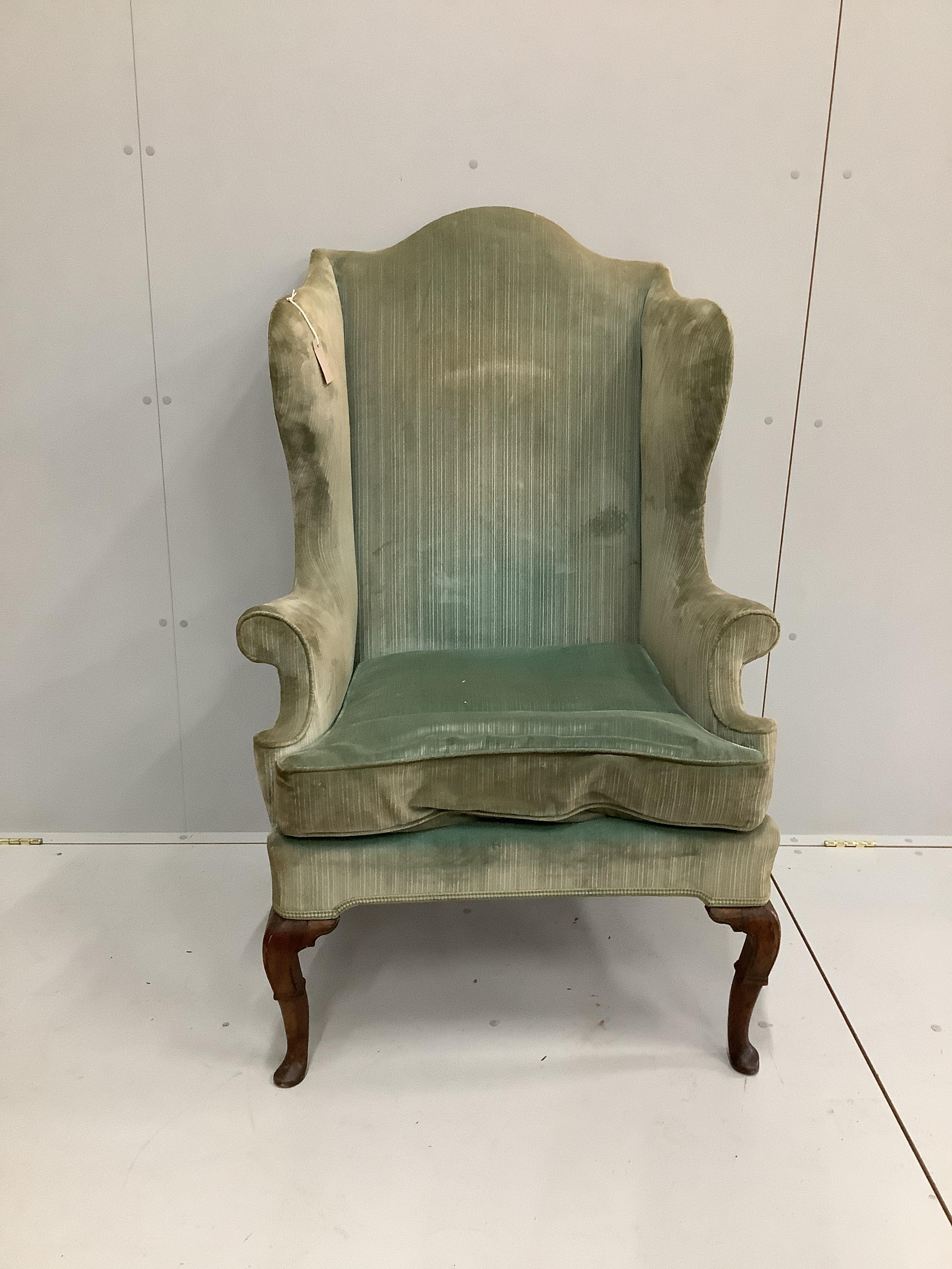 An 18th century upholstered wing armchair on carved walnut cabriole legs, width 80cm, depth 70cm, height 126cm.